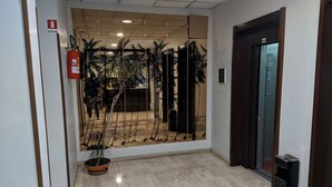 Corredor com extintor, planta em vaso e elevador.