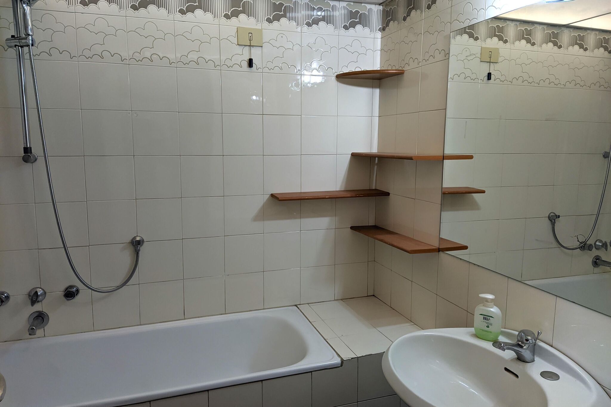 A bathroom with a bathtub, a sink, and a shower. There are wooden shelves and a mirror.