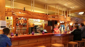 Una zona de bar con barra de madera, taburetes y estantes llenos de botellas y vasos.