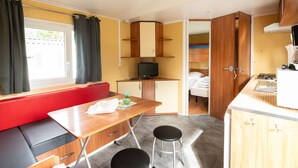 Una habitación compacta con kitchenette, una zona de comedor con mesa y taburetes, un banco rojo y una cama en la habitación contigua.