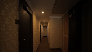Un pasillo tenuemente iluminado con paredes y puertas decoradas, que conduce a una habitación con la puerta cerrada.
