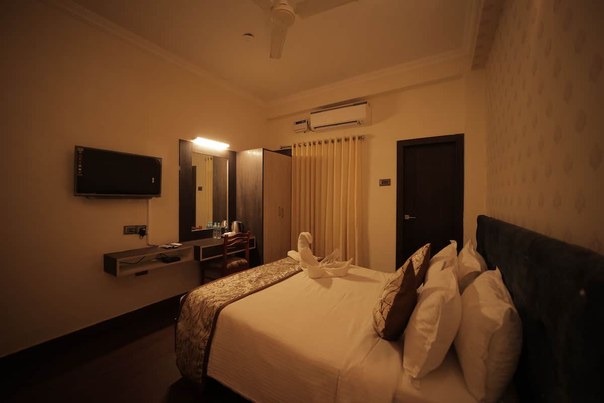 Una habitación de hotel con cama, escritorio, silla, televisor y aire acondicionado.