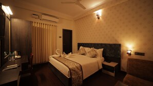 Una habitación de hotel con cama, mesita de noche, silla, escritorio y ventilador de techo.