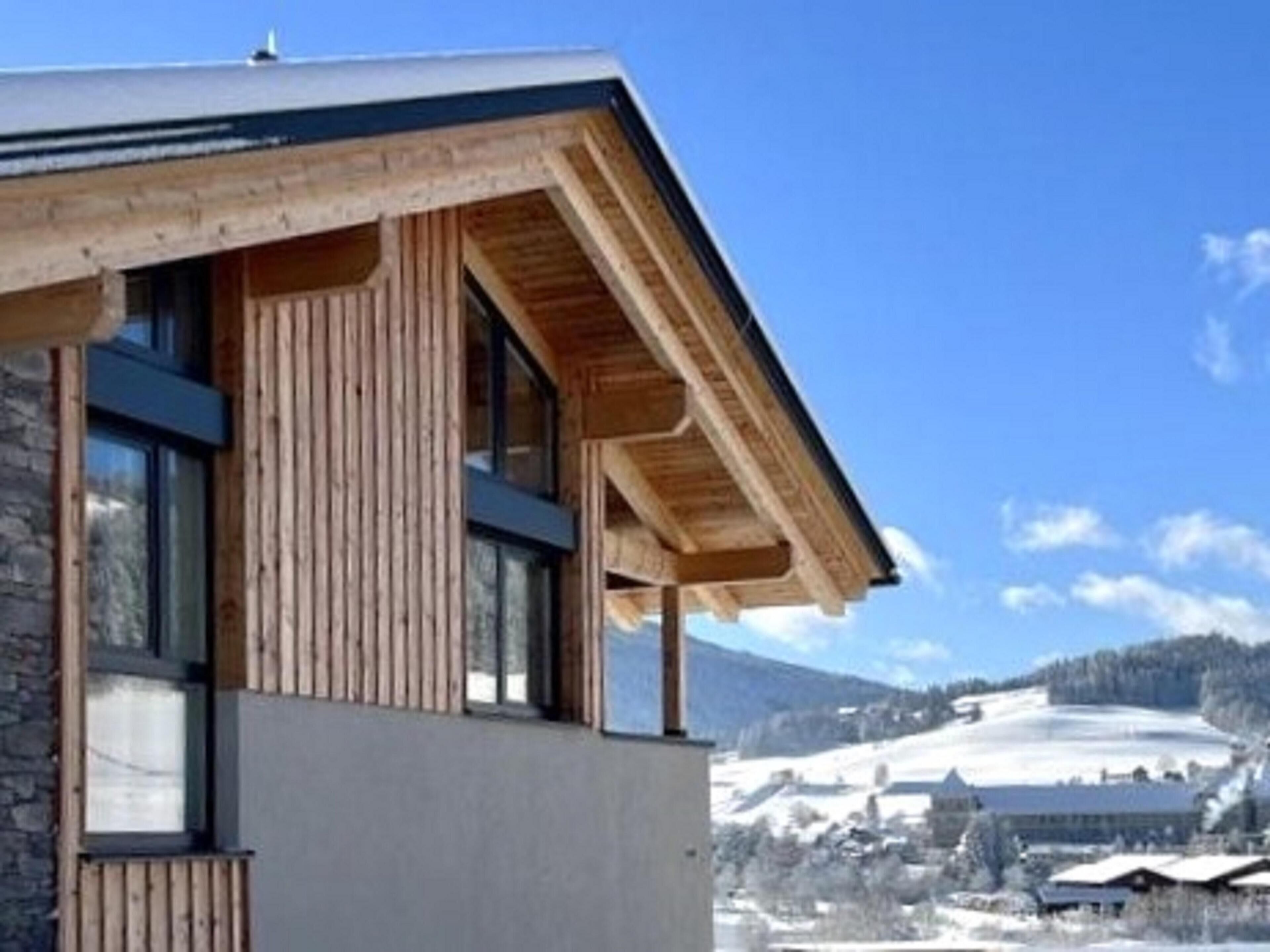 A modern building with a stone facade and wooden beams, overlooking a snowy landscape with a clear sky.