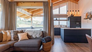 Un salon moderne avec un canapé d’angle, un panier en osier et une vue sur une cuisine dotée de meubles sombres et d’un four à micro-ondes.