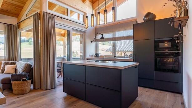 Une cuisine moderne dotée d’un îlot central, d’un plafond en bois et de grandes fenêtres.