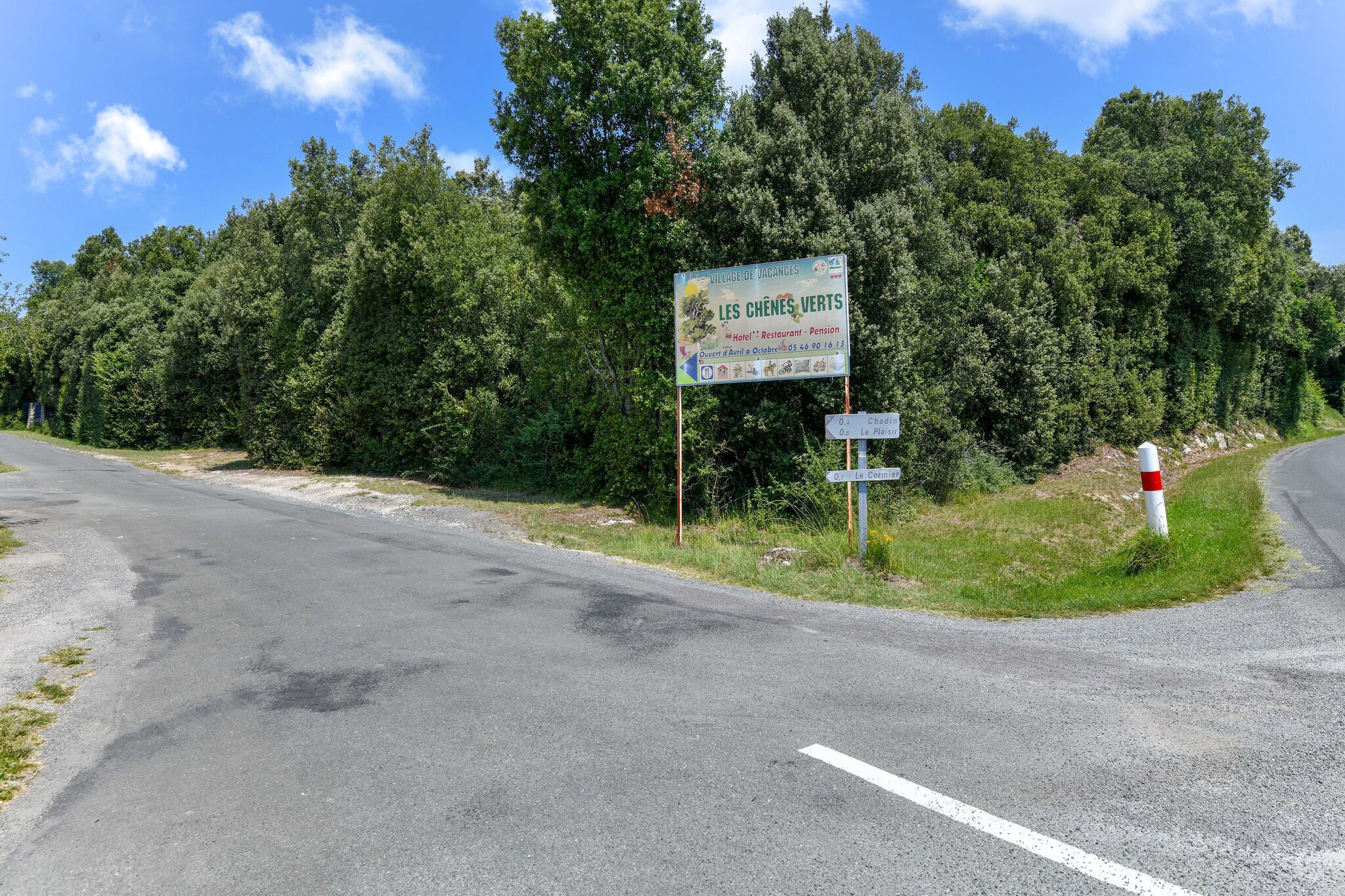 A road sign for 'Les Chênes Verts' with a restaurant, pension, and a contact number.
