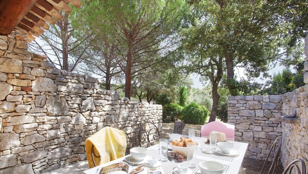 A stone wall, a table set for breakfast, and a book open on the table.