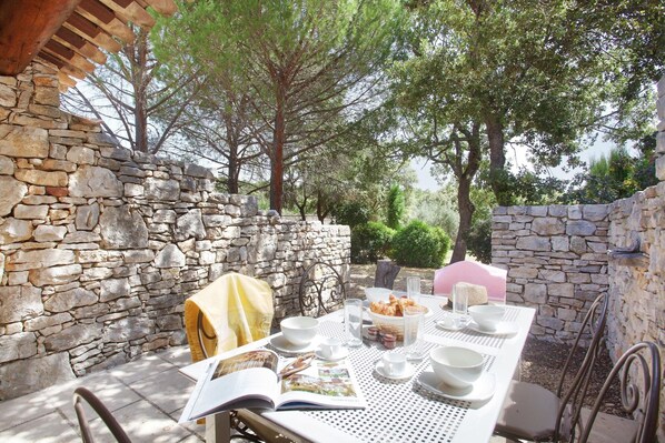 A stone wall, a table set for breakfast, and a book open on the table.