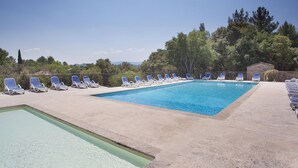 Et rektangulært swimmingpool med liggestole placeret omkring det, omgivet af en stenterrasse og træer.