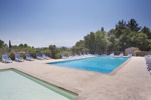 Ein rechteckiger Pool mit Liegestühlen, umgeben von einer Steinterrasse und Bäumen.