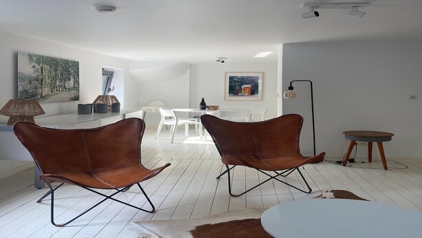 Un salon moderne avec un plancher blanc, deux fauteuils en cuir marron, une table à manger blanche et une petite table ronde.