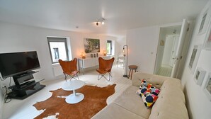 Un salon moderne doté d’un téléviseur à écran plat, d’un canapé en cuir, de deux fauteuils en cuir, d’une table basse ronde et d’un tapis en peau de vache.