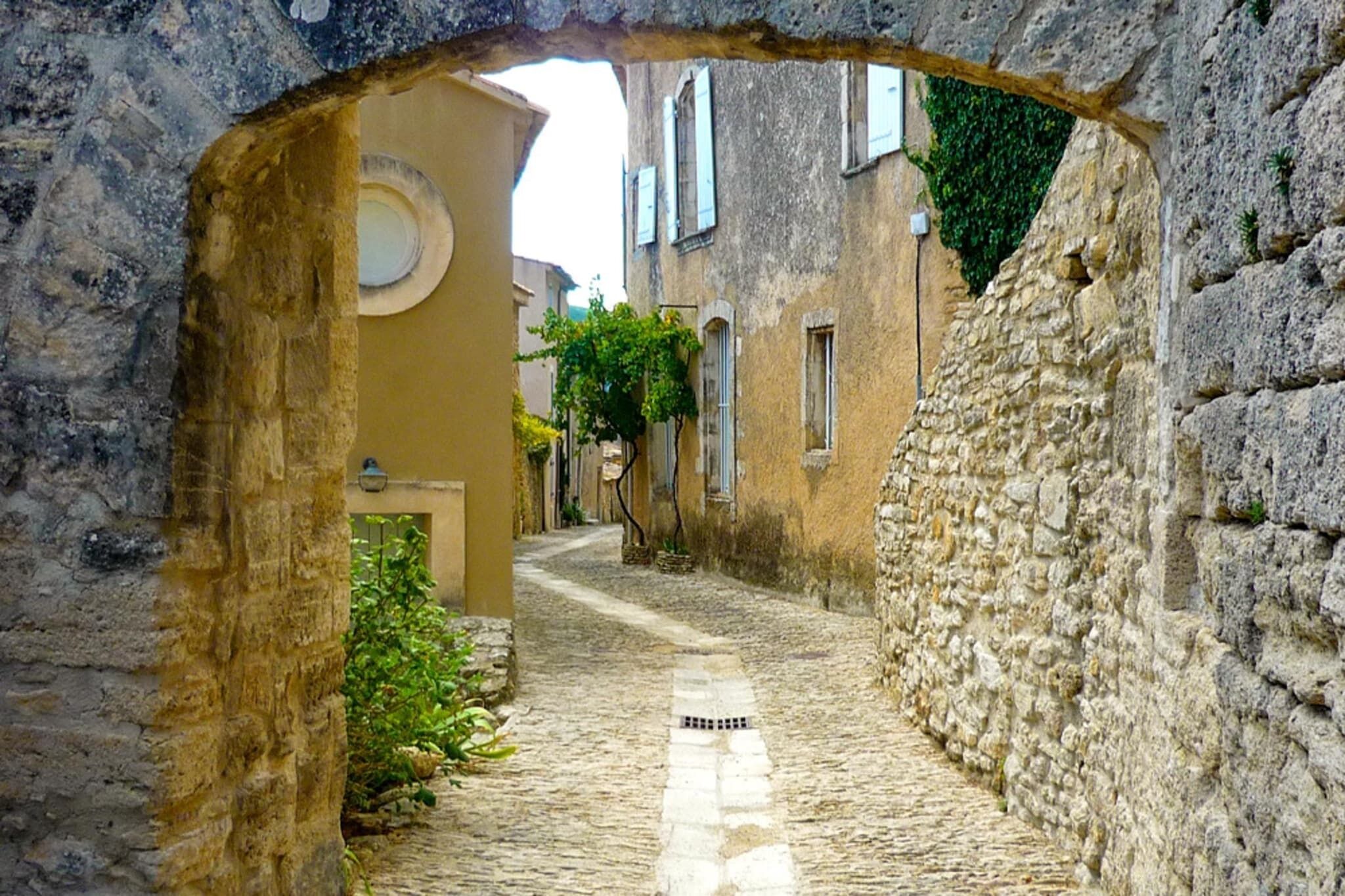 A narrow cobblestone alleyway framed by stone walls, leading to a building with a round window and a door.