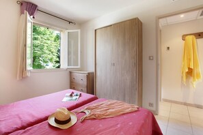 Un dormitorio con dos camas, un armario, una ventana con cortinas y una toalla amarilla colgada en la pared.