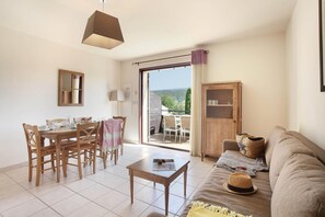 A living room with a dining area, a sofa, a table, and a view of the outdoors.