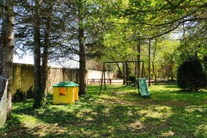 A backyard with a playhouse, a swing set, and a slide.