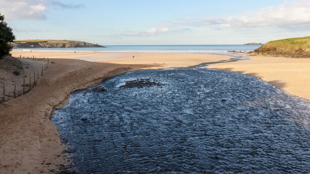 A beach with a rocky shoreline, a sandy path, and a view of the sea and distant hills. - 6B The Mews (Padstow)