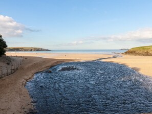 A beach with a rocky shoreline, a sandy path, and a view of the sea and distant hills.