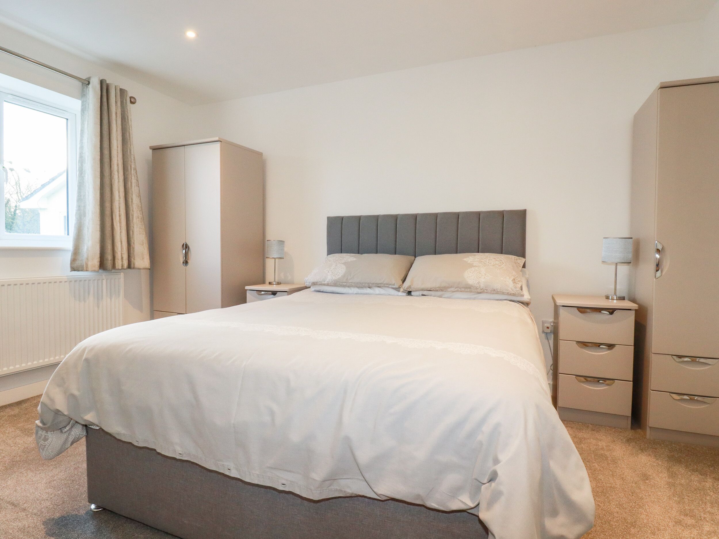 Un dormitorio ordenado con una cama grande, mesitas de noche y un armario.