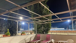 Un espacio al aire libre con sillas, una mesa y una estructura cubierta, con vista a un campo deportivo por la noche.