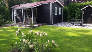 Une maison noire avec un toit rouge, une terrasse couverte et un petit jardin agrémenté de fleurs blanches.