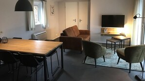 A modern living room with a wooden dining table, two sofas, a TV, and a small side table. - Peaceful Forest Chalet (Elst)