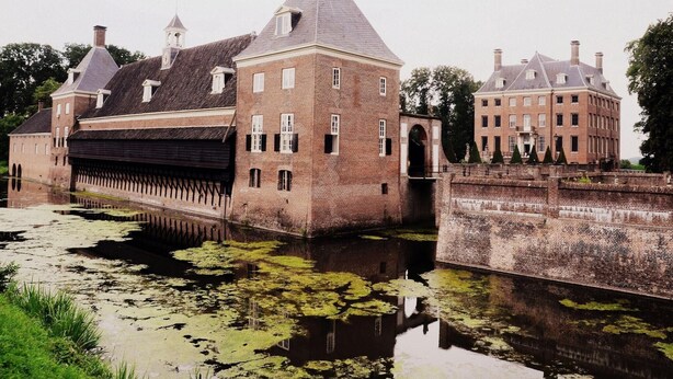 A historic building with a large water body in front, featuring a bridge and a canal. - Peaceful Forest Chalet (Elst)