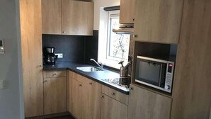 A modern kitchen with wooden cabinets, a stainless steel sink, and a built-in microwave. - Peaceful Forest Chalet (Elst)