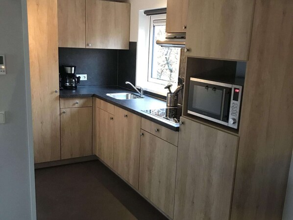 Cozinha moderna com armários de madeira, pia de aço inoxidável e micro-ondas embutido.