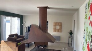 Ein modernes Wohnzimmer mit einem großen Kaminofen, gemütlicher Sitzgelegenheit und Blick ins Freie.