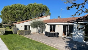 Ein modernes Haus mit Terrasse, Essbereich und einem großen Baum im Hintergrund.