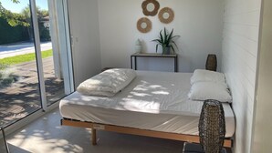 Ein modernes Schlafzimmer mit einem Bett, einem kleinen Tisch, einer Topfpflanze und dekorativer Wandgestaltung.