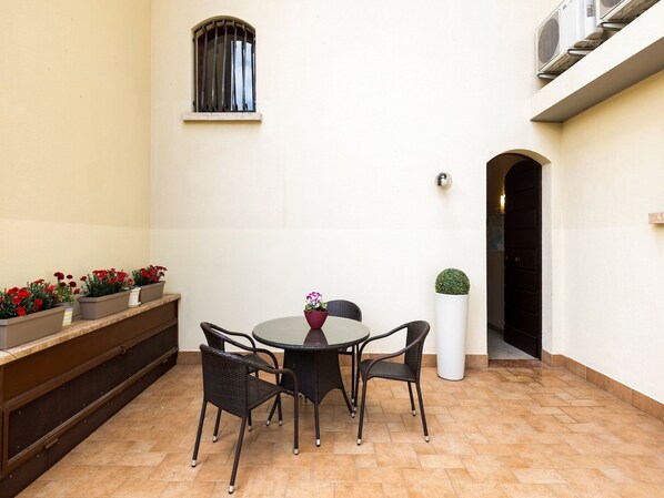 Un patio con una mesa redonda y cuatro sillas, una ventana pequeña y plantas en macetas.