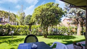 A patio with a table and chairs, a small table with a tissue box, and a view of a well-maintained garden with various trees and shrubs.