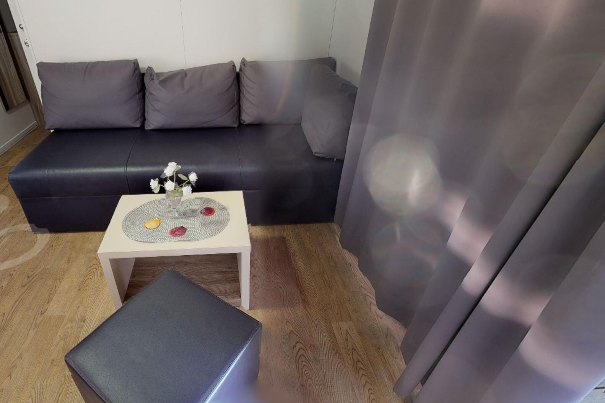 Una sala de estar con un sofá de cuero oscuro, una mesita blanca con una bandeja decorativa y un otoman gris.