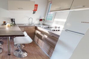 A modern kitchen with wooden cabinets, a stainless steel refrigerator, and a bar stool.