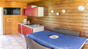 Una cocina compacta con paredes de madera, un mueble rojo y blanco, un lavamanos y una mesa con mantel azul.