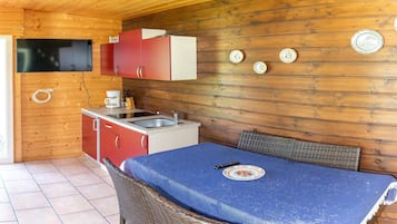 Een kleine keuken met houten wanden, een rode en witte kast, een spoelbak en een tafel met een blauwe tafelkleed.