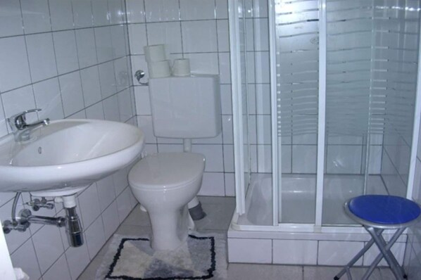 Un baño con lavamanos blanco, inodoro y cabina de ducha con paredes de vidrio.