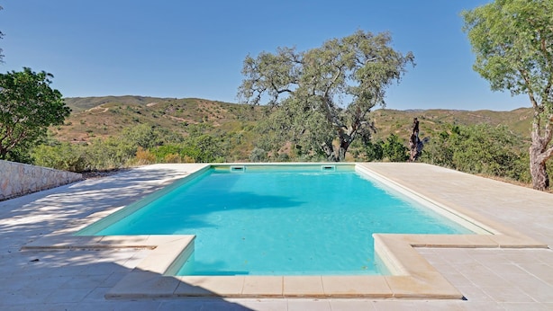 Ein rechteckiger Swimmingpool mit klarem, blauem Wasser, umgeben von einer Steinmauer und einer gepflasterten Terrasse.