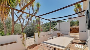 Eine Terrasse im Freien mit Tisch und Stühlen, umgeben von weißen Mauern und Pflanzen.