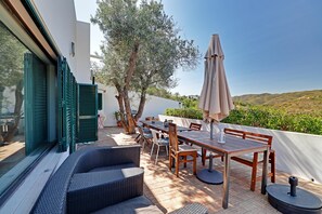 Une terrasse avec une table et des chaises, un canapé en osier et une vue sur les collines.