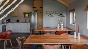 A modern kitchen with white cabinets, a wooden ceiling, and a dining area with a wooden table and chairs. - Lodges in Drenthe with Scenic Meadow Views (Ruinerwold)