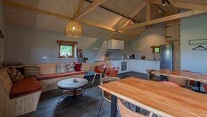 A cozy interior with a wooden bench, round table, and chairs, a kitchen area, and a hanging light fixture. - Lodges in Drenthe with Scenic Meadow Views (Ruinerwold)