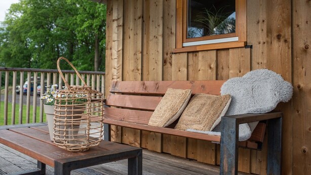 A wooden deck with a bench, a wicker basket, and a window overlooking greenery. - Lodges in Drenthe with Scenic Meadow Views (Ruinerwold)