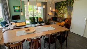A modern living room with a wooden dining table, chairs, a sofa, and a television. - Holiday Home in Lemele near Nature Reserve (Overijssel)