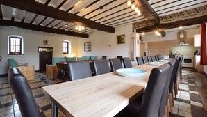 A dining area with a long wooden table and black chairs, a kitchen in the background, and a checkered floor. - Luxury Holiday Home with Sauna (Melreux-Hotton)