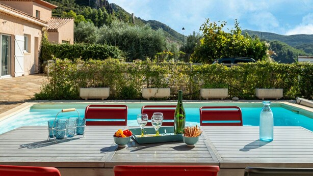 A poolside table with drinks and snacks, surrounded by a pool and a mountainous backdrop. - House in the south of France with private pool (Roquebrun)