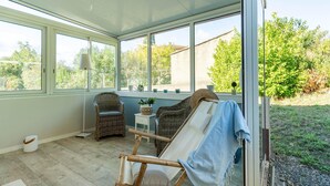 A sunroom with large windows, wicker furniture, and a view of the garden. - House in the south of France with private pool (Roquebrun)